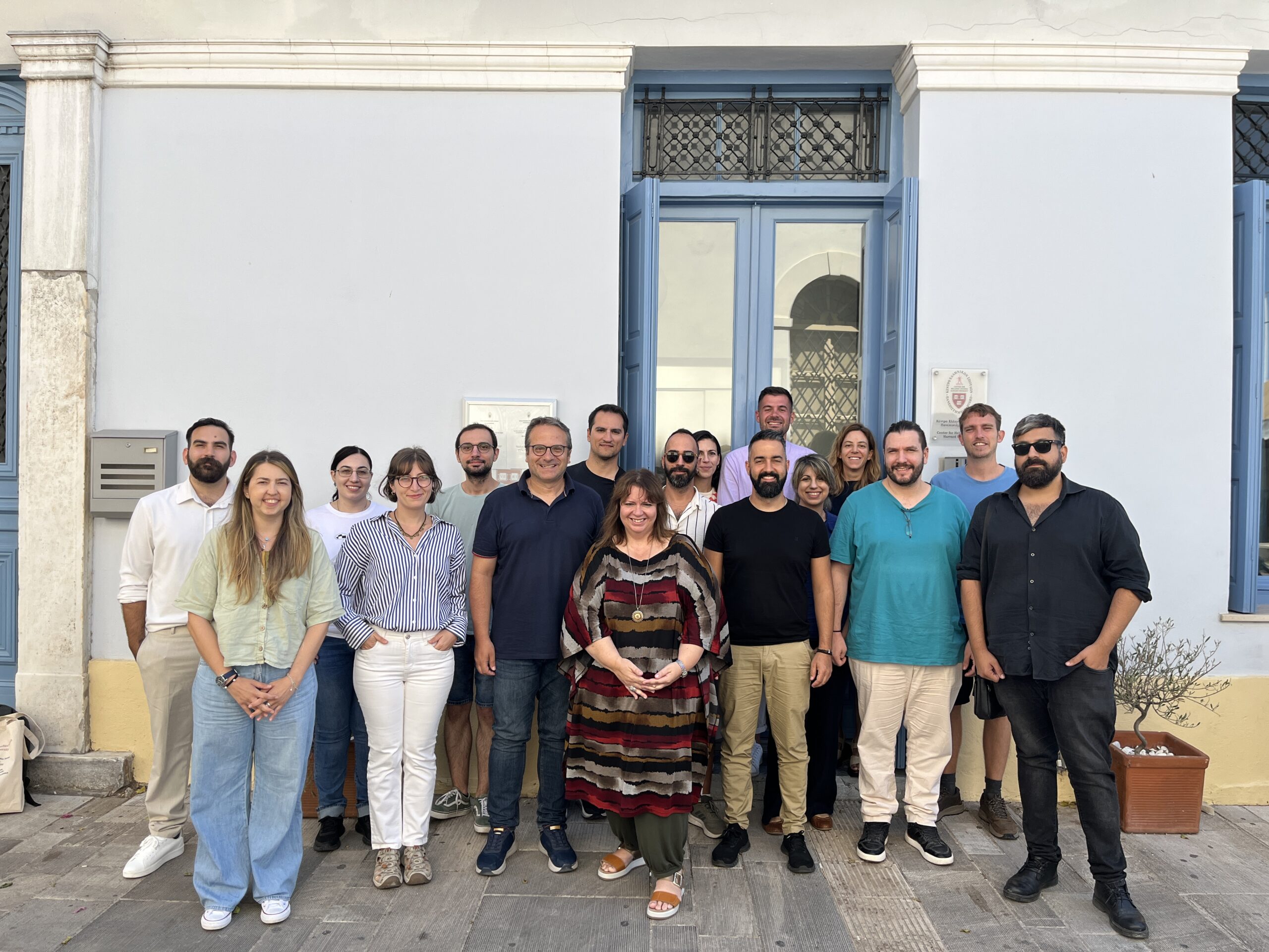 A group of about 20 people pose for a group photo on a sunny day outside of a neoclassical building.