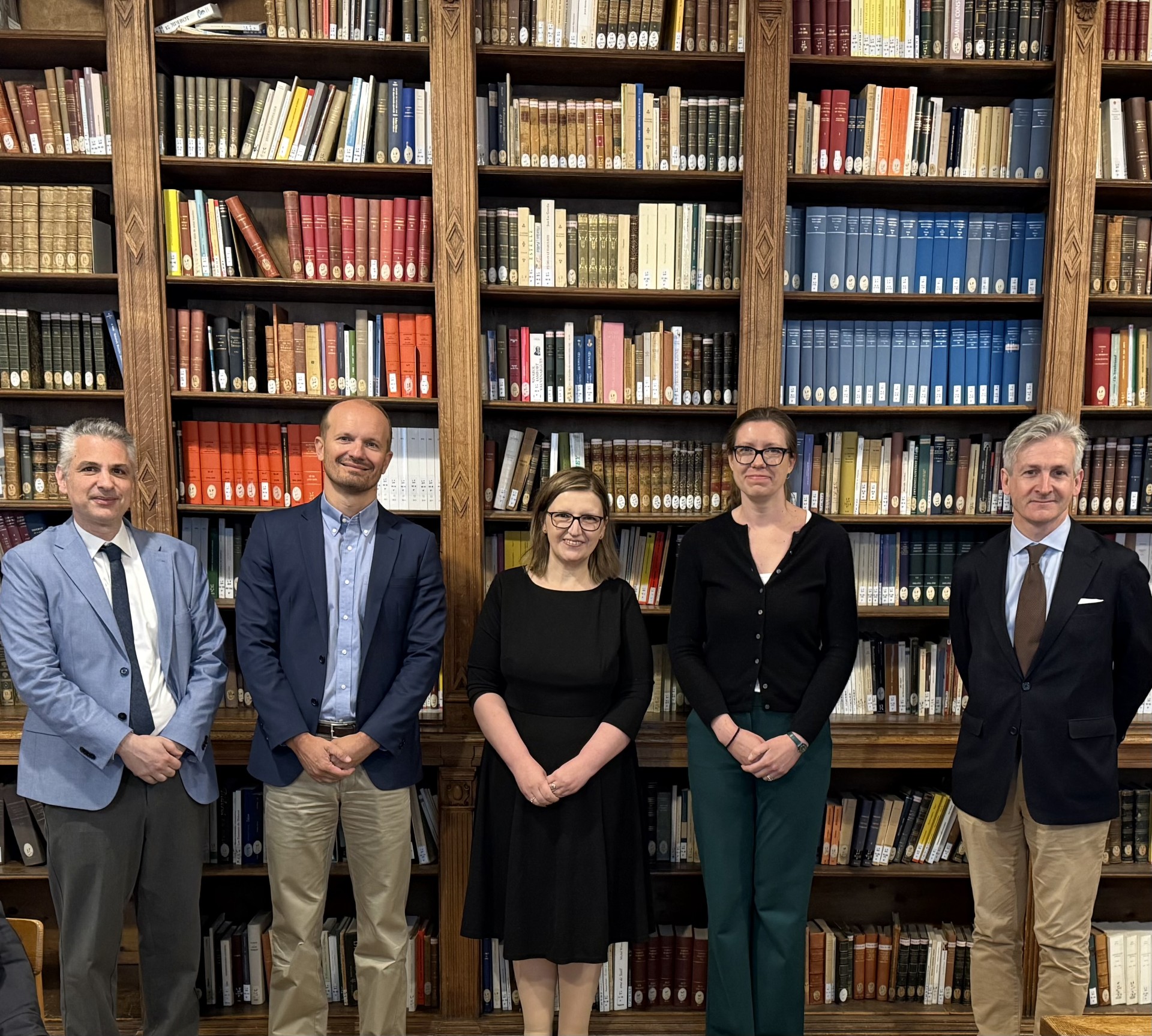Five people standing in front of tall bookshelves in a library.
