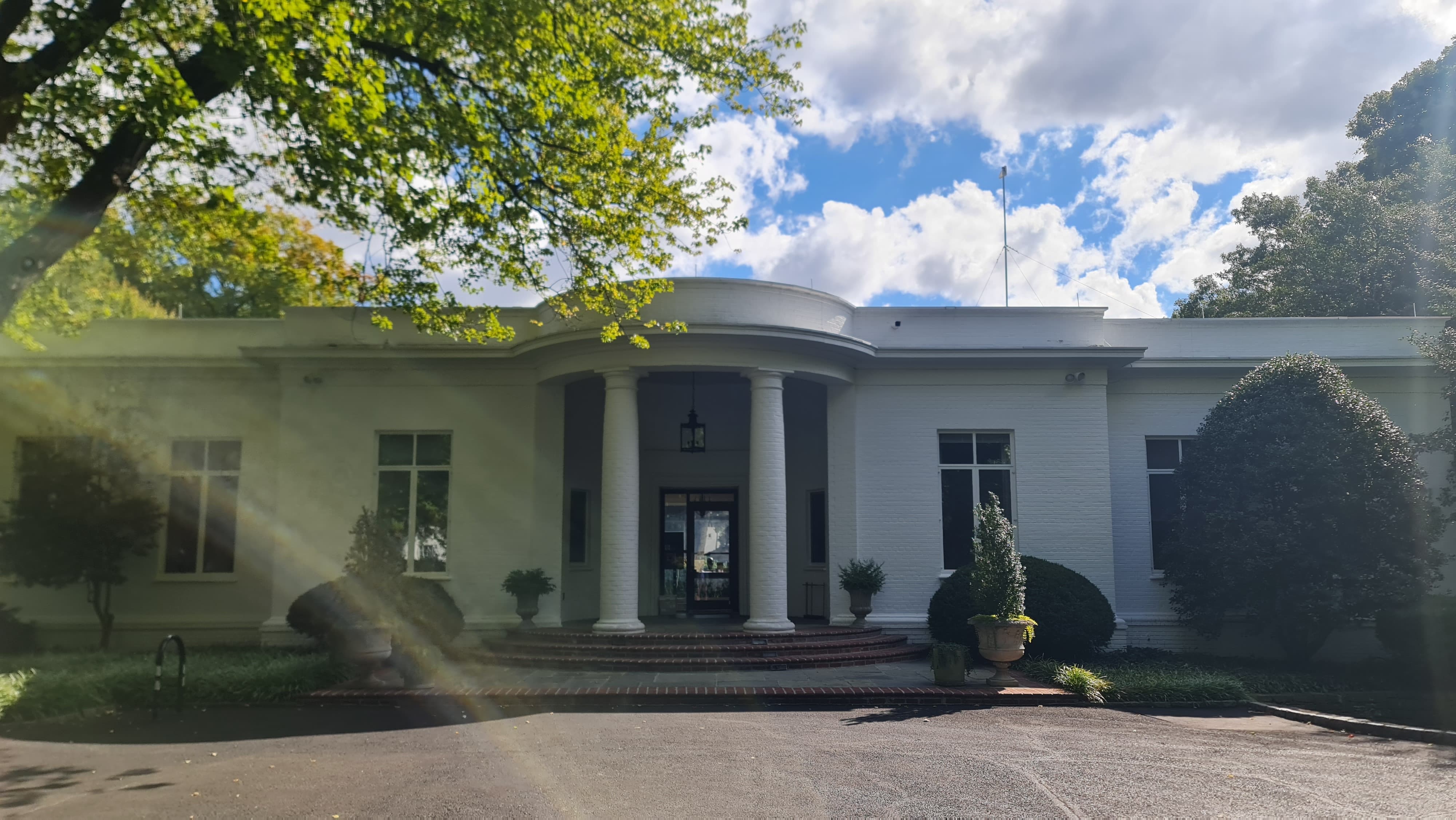 A front entrance in the form of a semicircular white structure amidst trees of vibrant green hues.