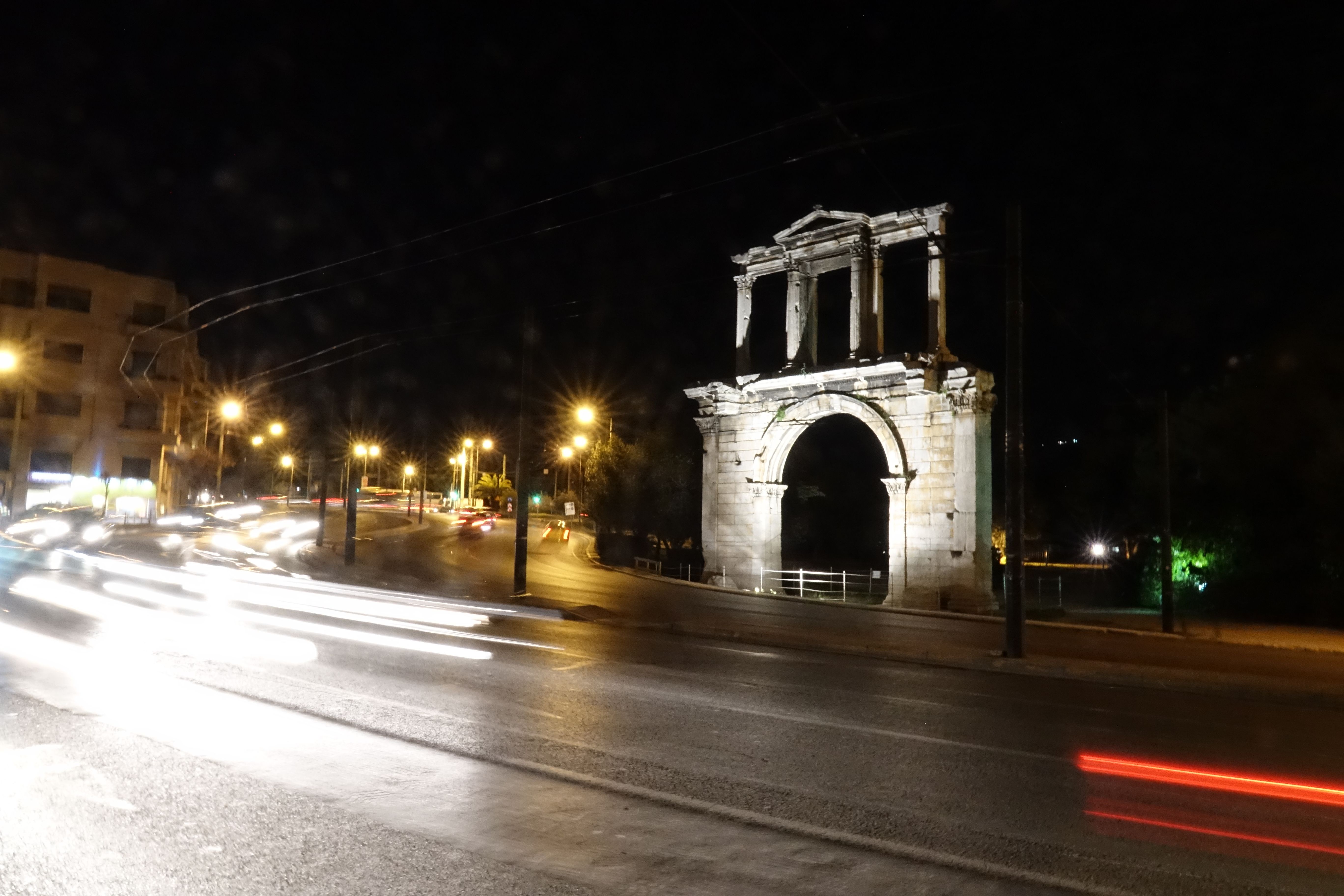Night-view of the Arch of Hadrian in Athens in the background of a busy street with car lights.