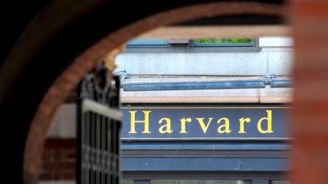 The word “Harvard” is revealed in golden letters, glimpsed through an arched gateway.