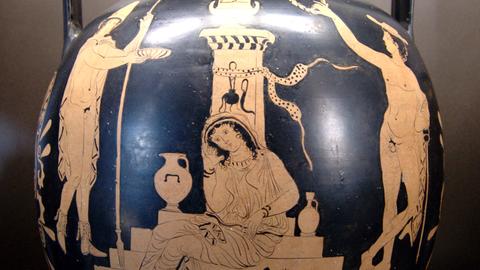 Ancient Greek red‑figure vase showing a mourning woman seated on the steps of a tomb, flanked by two standing figures making offerings, with vases and a serpent depicted at the base.