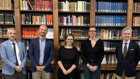 Five people standing in front of tall bookshelves in a library.
