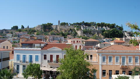 Historic hilltop fortress overlooking a town with colorful buildings and red-tiled roofs under a clear blue sky.