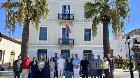Group portrait of the workshop participants outside the CHS Greece building in Nafplio, between two palm trees.