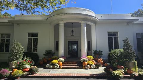 The entrance to the Center for Hellenic Studies in Washington, DC, a white building with a columned portico, decorated with autumn pumpkins and chrysanthemums.