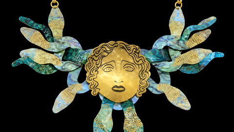 A gold-toned statement necklace in the shape of Medusa's head, with snakes for hair, against a plain background.