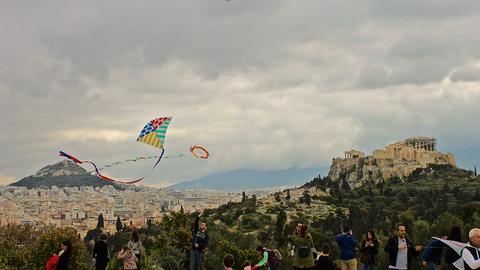 Group of people flying kites with the Acropolis hill showing in the background.