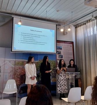 Students present a research project to an audience in a lecture hall.