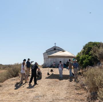 Researchers gathered near a small chapel, preparing fieldwork equipment in a dry rural setting.