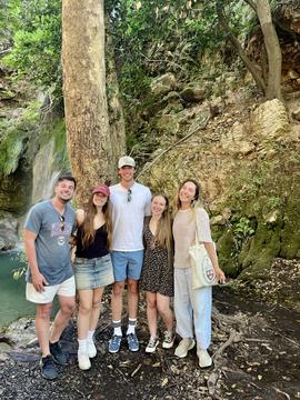 Group photo beside a waterfall in a wooded area, showing participants during an excursion.