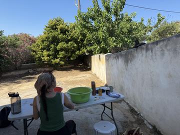 Workshop participant seated at an outdoor worktable, with archaeological materials and equipment nearby.