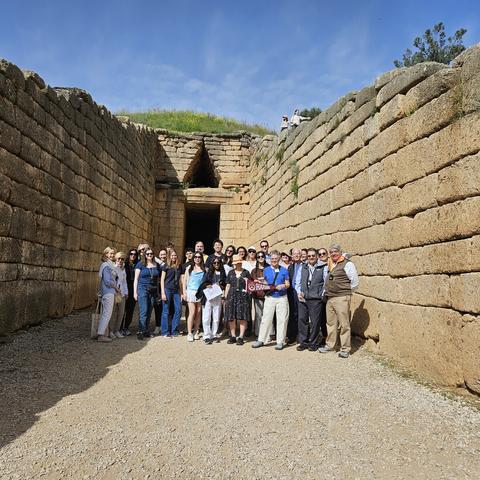 A group poses together inside the Treasury of Atreus, a large stone structure with high walls and a triangular entrance.