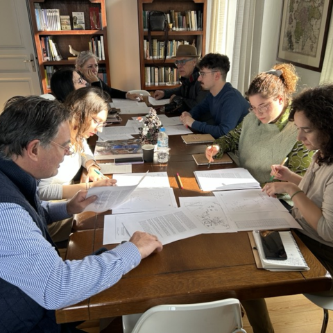 A small group reviews documents and takes notes around a well-lit table in a library setting.