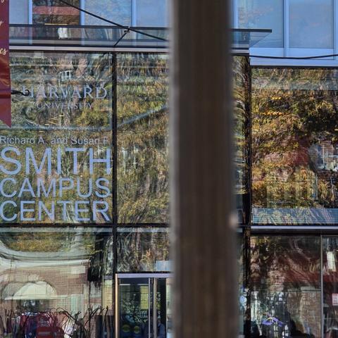 Glass-fronted Smith Campus Center with reflections of trees and "Harvard University" signage.
