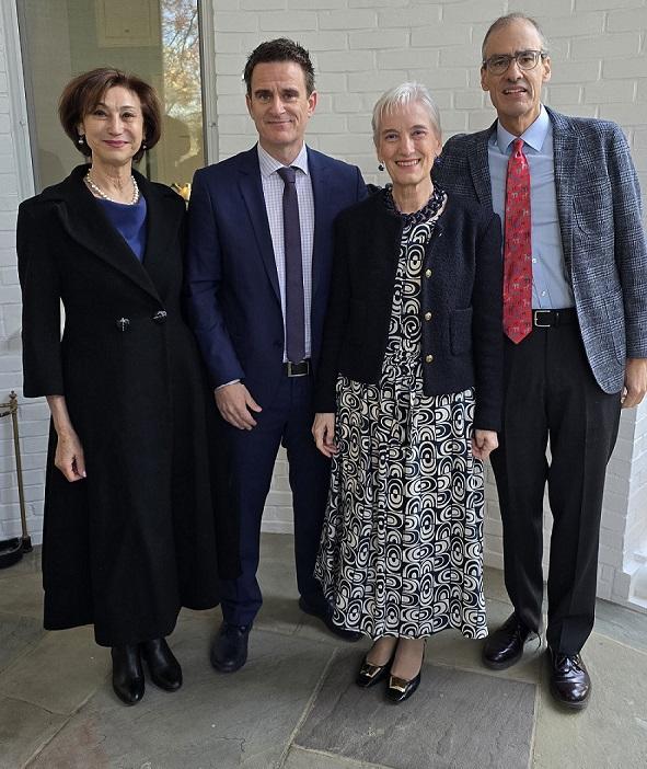 Four people are posing together in front of a white brick wall, dressed in formal attire.
