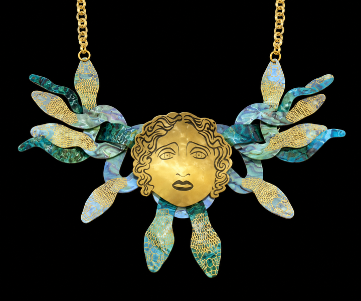 A gold-toned statement necklace in the shape of Medusa's head, with snakes for hair, against a plain background.