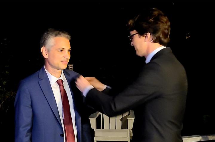 Man in black suit decorating man in dark blue suit.