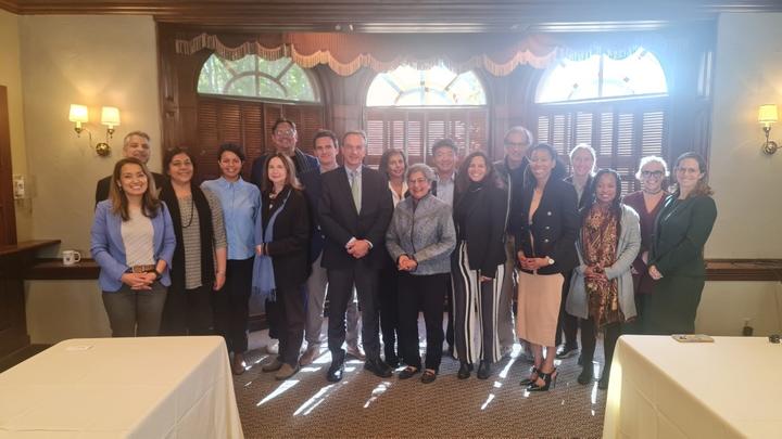 About 30 people smiling at the camera while standing in a room.