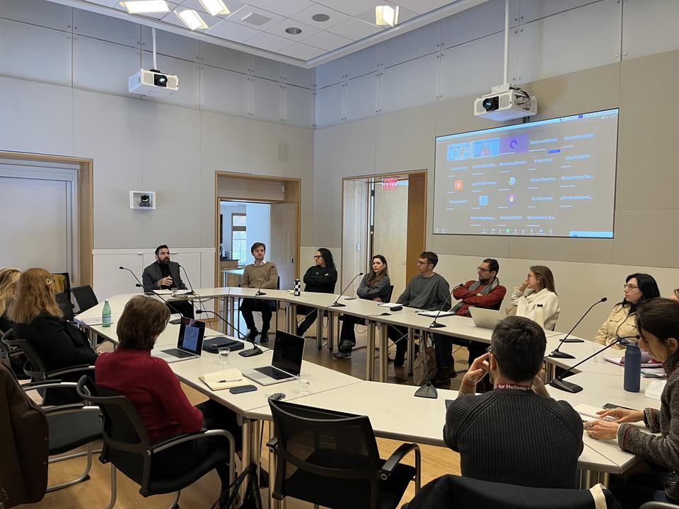 Round‑table meeting in a modern conference room with participants discussing while others join via video call on a large screen.