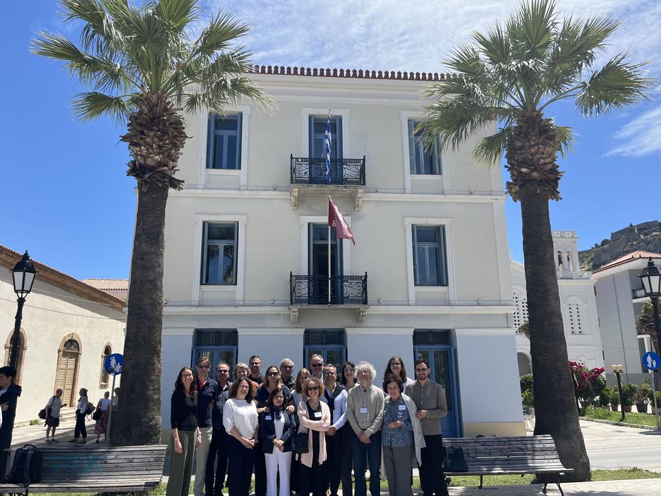 Small group of conference participants posing in front of a white neoclassical building framed by two palm trees.