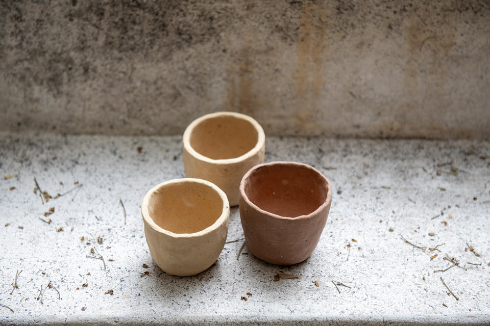 Three small handmade clay cups on a speckled concrete surface.