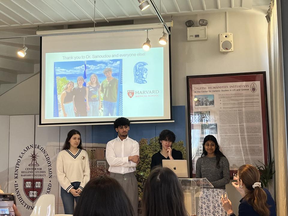 Student team presents their project at the Genomic Medicine Course, with a slide thanking Dr. Sanoudou and CHS displayed behind them.