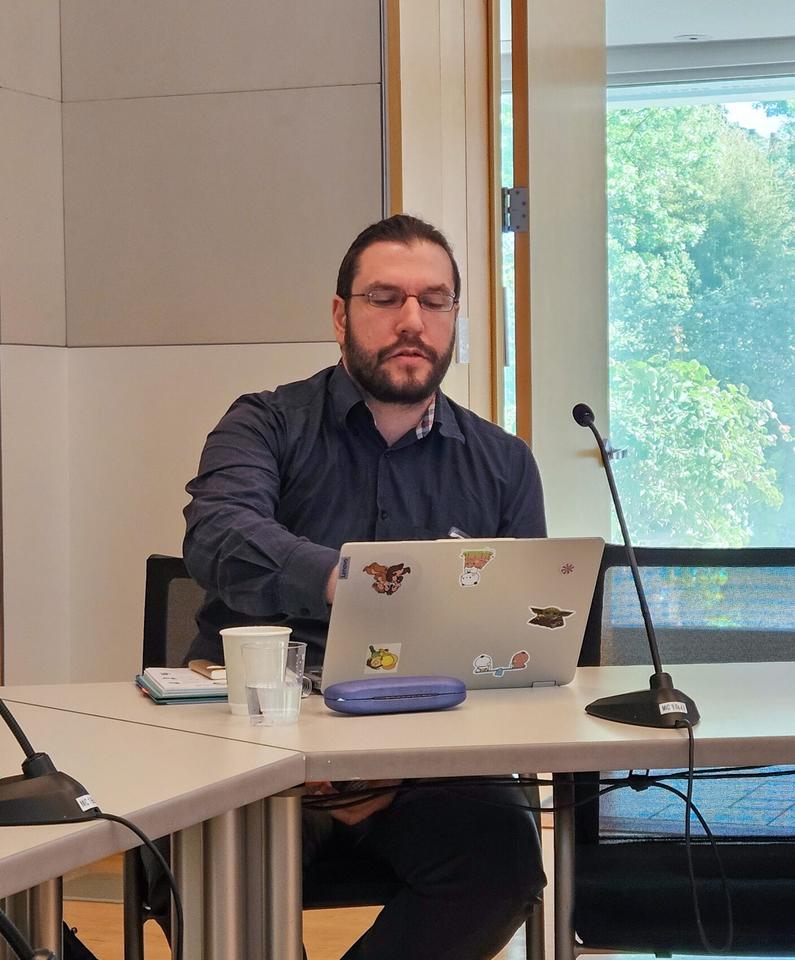 Person seated at a conference table in front of a laptop with a notebook beside them.