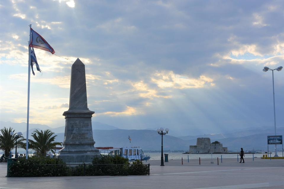A town square with an obelisk-shaped monument that receives a few sunrays on a cloudy day.