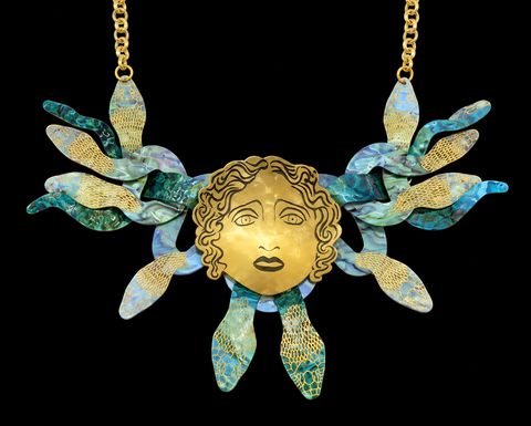 A gold-toned statement necklace in the shape of Medusa's head, with snakes for hair, against a plain background.