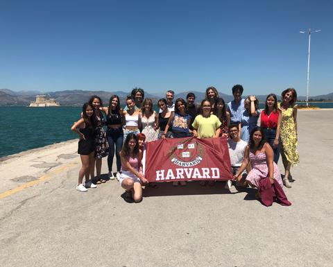 HSSP 2022 Group in front of the Port of Nafplio holding a Harvard flag.