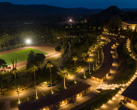 A night aerial photograph of the facilities of the International Olympic Academy in Ancient Olympia. Illuminated, the buildings span three levels within a lush landscape, accompanied by a striking track and field stadium.