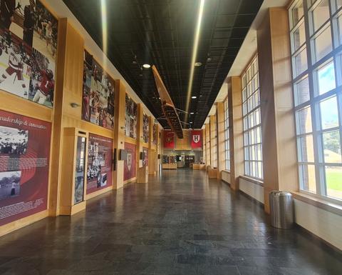A spacious corridor with windows on the right and a wall with pictures of athletes from various sports on the left.