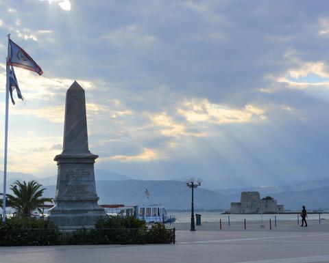 A town square with an obelisk-shaped monument that receives a few sunrays on a cloudy day.