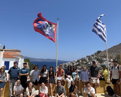 The 2024 Harvard Summer School cohort gathered at the Koundouriotis Mansion on the island of Hydra. In the background, the sparkling sea complements the amphitheater-like arrangement of houses, creating a picturesque scene on a sunny morning.